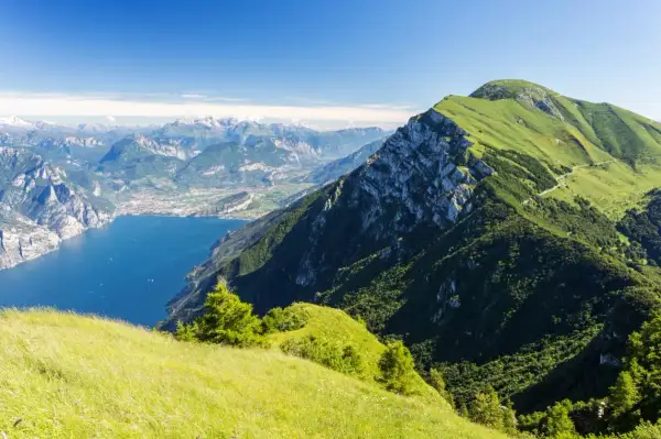 Panoramica mozzafiato dal Monte Baldo: lago blu intenso, montagne verdi e un cielo limpido.