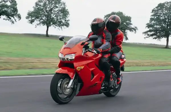 Dwie osoby w czerwonych kombinezonach jadą na czerwonym motocyklu Honda VFR 800.