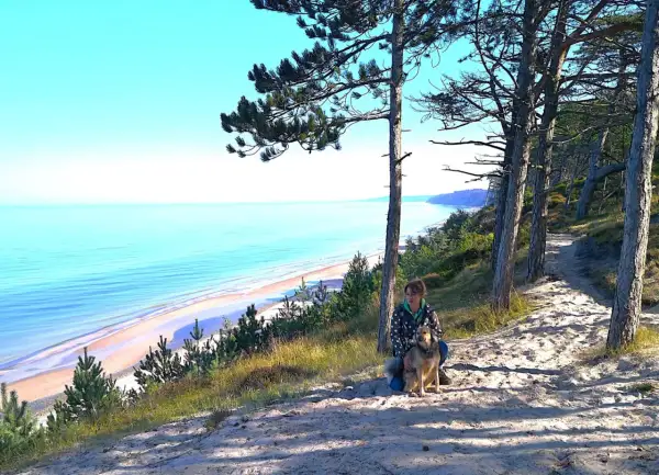 Frau mit Hund auf einem sandigen Pfad mit Blick auf die polnische Ostsee.