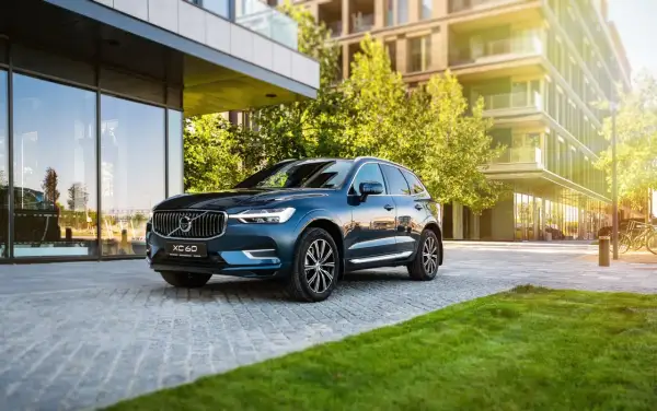 Elegancki, ciemnoniebieski Volvo XC60 zaparkowany przed nowoczesnym budynkiem. Wiele osób szuka volvo xc60 opinie, by podjąć decyzję o zakupie.