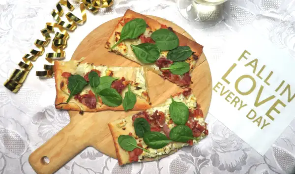 Prosciutto pizza med färsk spenat på en träskärbräda, omgiven av guldfärgad serpentin. En perfekt bit att "fall in love" med.
