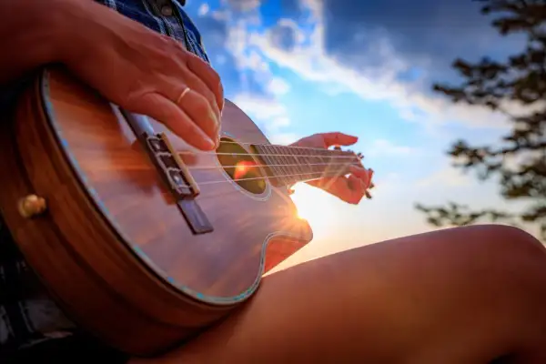 Słońce zachodzi, a ja uczę się, jak się gra na ukulele. Dźwięki instrumentu unoszą się w powietrzu.