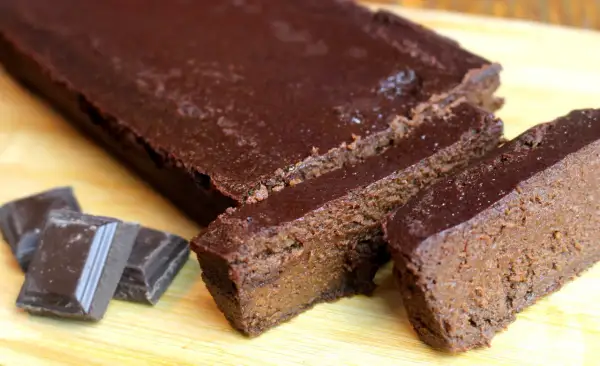 Un délicieux gâteau chocolat compote, coupé en tranches, avec des carrés de chocolat à côté.