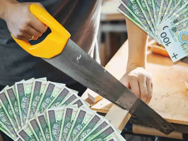 Cieśla tnie drewno piłą, a wokół leżą banknoty 100 zł. Zarobek rzemieślnika.