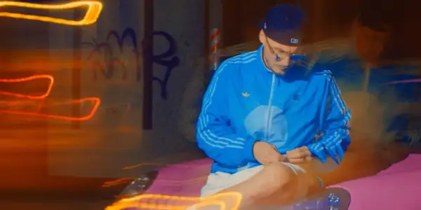 Mężczyzna w niebieskiej kurtce i czapce siedzi na tle nocnego miasta z neonowymi światłami.