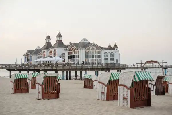 Plaża w Stralsundzie w Niemczech z charakterystycznymi koszami plażowymi i molo z białą budowlą.