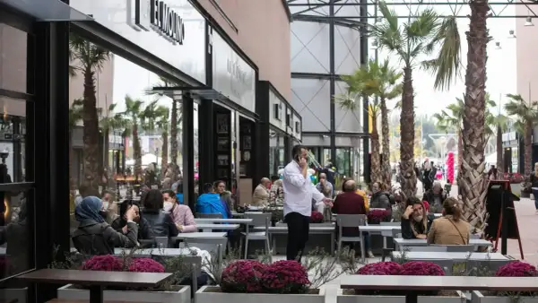Gente disfrutando en los restaurantes de la torre outlet, rodeados de palmeras y flores.