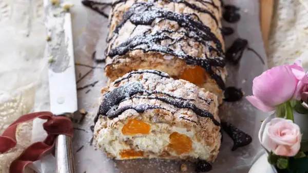 En läcker budapestbakelse med vispgrädde, frukt och chokladdrizzle, pudrad med florsocker.