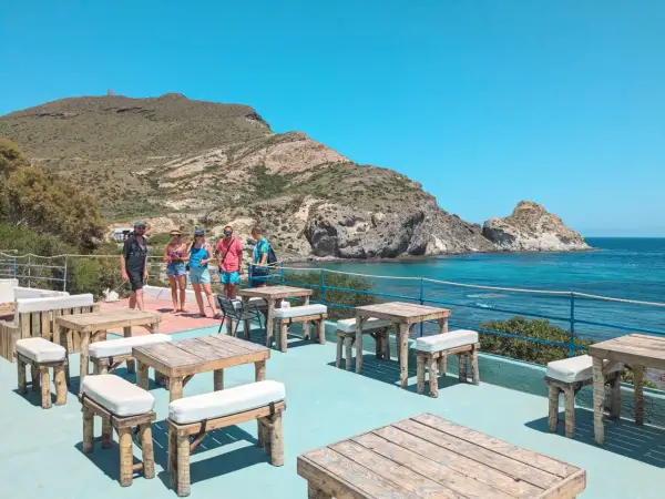Terraza del cala higuera restaurante con mesas de madera y vistas al mar. Un grupo de amigos disfruta del sol.