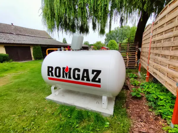 Biały zbiornik na gaz ziemny z napisem ROMGAZ, podłączony do instalacji ogrzewania gazowego z butli.