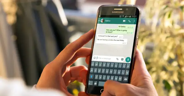 Dłonie trzymają smartfon z otwartym WhatsAppem. Widoczna jest rozmowa i klawiatura, co może pomóc w nauce jak zainstalować WhatsApp.