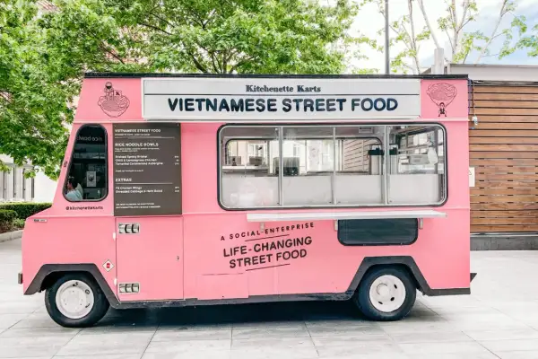 Un food truck rosa brillante, "Kitchenette Karts", offre "Vietnamese Street Food" e cibo che cambia la vita.