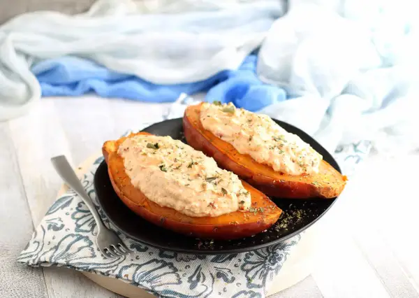 Due patate dolci al forno, tagliate a metà e farcite con un cremoso ripieno, guarnite con erbe aromatiche.