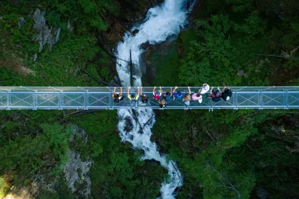 Un gruppo di persone ammira la cascata nel **Val di Rabbi** da un ponte sospeso.