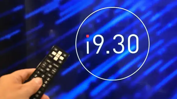 Dłoń z pilotem przed ekranem z godziną 19.30. Czy zmiana godziny emisji programu wpłynęła na oglądalność?