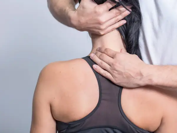 Hände eines Therapeuten massieren den Nacken einer Frau, die unter starken Nackenschmerzen leidet.
