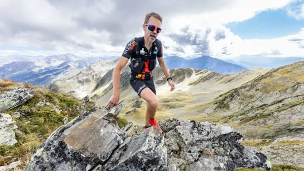 Un traileur en plein effort sur un sentier rocailleux, le regard déterminé, incarne l'ultra spirit dans un paysage montagneux spectaculaire.