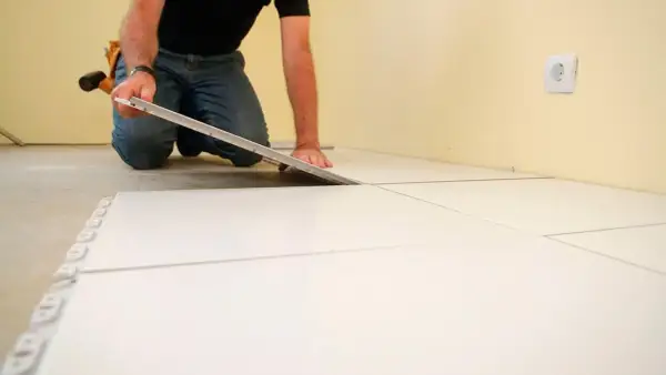 Hombre colocando baldosas blancas, un paso clave para como poner suelo porcelanico.