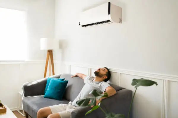 Un homme se repose sur un canapé sous la climatisation, ignorant les effets néfastes de la climatisation sur la santé et l'environnement.