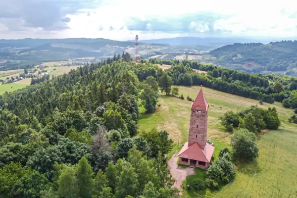 Kamienna wieża widokowa na wzgórzu, otoczona lasem i polami, oferuje wspaniałe widoki na krajobraz Dolnego Śląska.