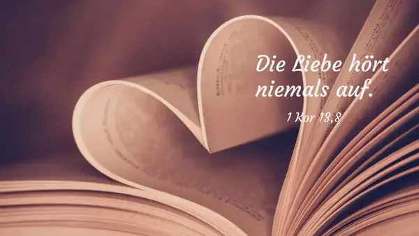 Ein aufgeschlagenes Buch formt ein Herz. Darauf steht: "Die Liebe hört niemals auf. 1 Kor 13,8". Bibelzitate über Liebe und Ehe.