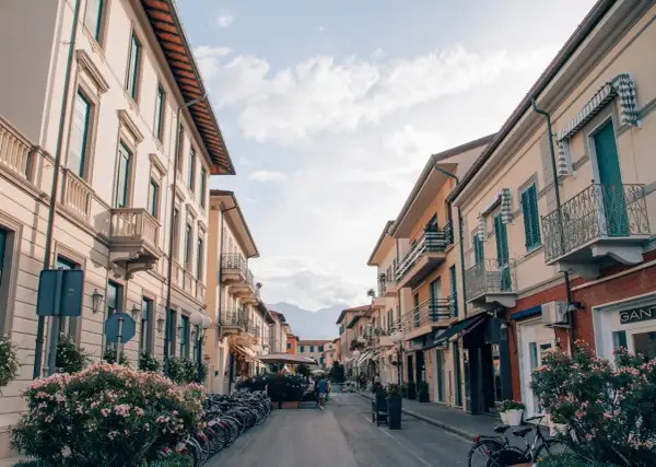 Strada pittoresca a Forte dei Marmi, Italia, con palazzi color pastello, balconi in ferro battuto e biciclette parcheggiate.