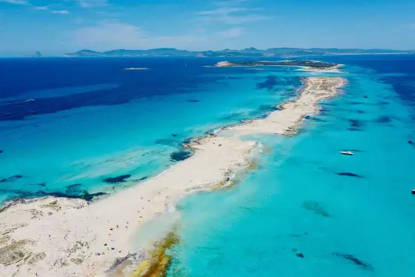 Arena blanca y aguas turquesas en la mejor playa de Formentera. Un paraíso con barcos y gente disfrutando del sol.