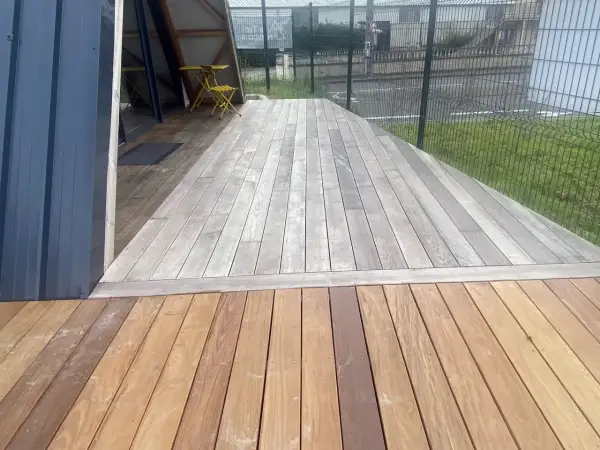 Terrasse en bois avec une partie grise, signe qu'il faut enlever le saturateur bois. Une table et une chaise jaunes sont visibles.