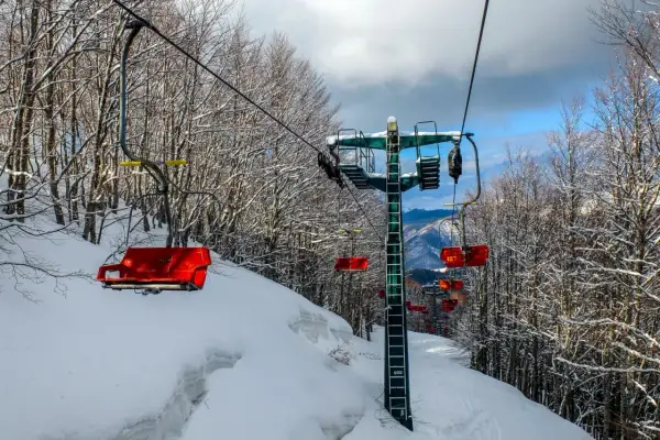 Seggiovia rossa su piste innevate ad Abetone, l'altitudine offre panorami mozzafiato tra alberi spogli coperti di neve.
