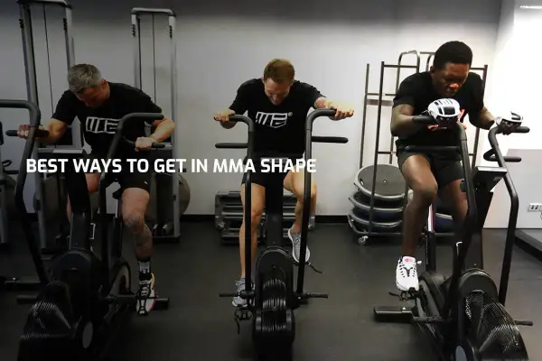 Three men with impressive fighters physique train on air bikes in a gym, showcasing their dedication to peak physical condition.