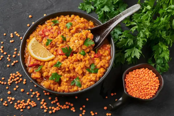 Rote Linsensuppe mit Zitrone und Petersilie, ein gesundes Gericht, das als Fettverbrenner Lebensmittel gilt. Daneben eine Schale roter Linsen.