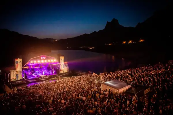 Gran concierto nocturno en el Pirineos Sur. Un mar de gente disfruta de la música bajo un cielo estrellado y montañas.