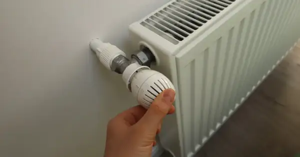 Ręka reguluje termostat grzejnika, gdy zaczynają grzać w blokach.