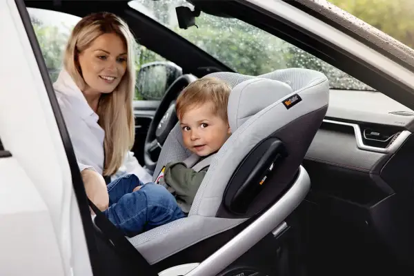Uśmiechnięta mama patrzy na synka w foteliku na przednim siedzeniu. Czy dziecko może jechać w foteliku na przednim siedzeniu? Tak, jeśli jest odpowiednio zabezpieczone.