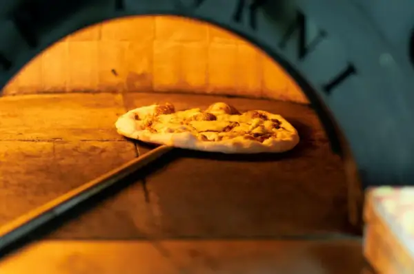 Pizza na łopacie w piecu, gdzie powstała pizza. Ciepło i tradycja wypieku.
