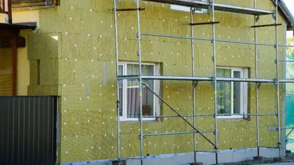 Budynek ocieplany wełną mineralną, widoczne rusztowania i okna. Tak powstaje wełna, która chroni dom.