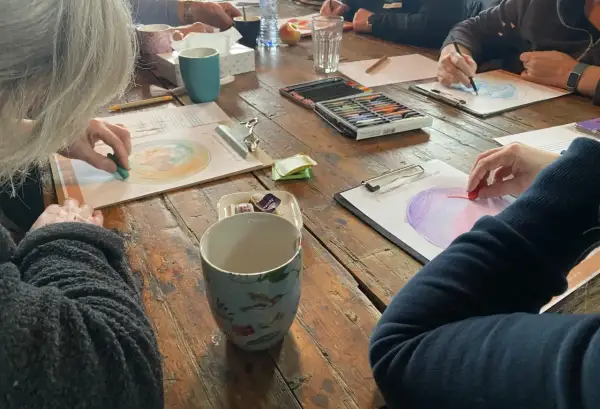 Creatieve workshop voor hsp mensen. Ze tekenen met pastelkrijt op papier, omringd door kopjes en kleurpotloden.