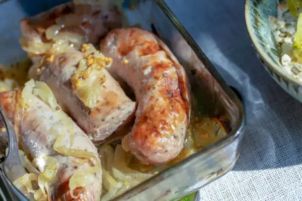 Soczysta biała kiełbasa pieczona z cebulą i musztardą w szklanym naczyniu.