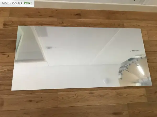 Un grand panneau de dibond miroir reflète le plafond et un mur blanc, posé sur un parquet en bois.