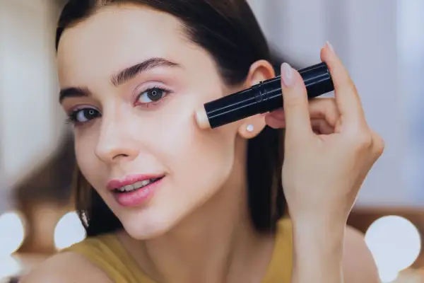 Donna applica il correttore, assicurandosi che il correttore deve essere più chiaro del fondotinta per un look luminoso.
