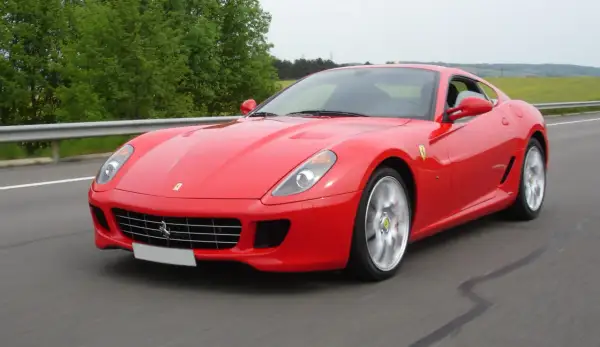 Czerwone Ferrari 599 pędzi po drodze, otoczone zielenią.