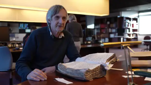 Un homme consulte un livre ancien, peut-être une source pour les meuse archives en ligne.
