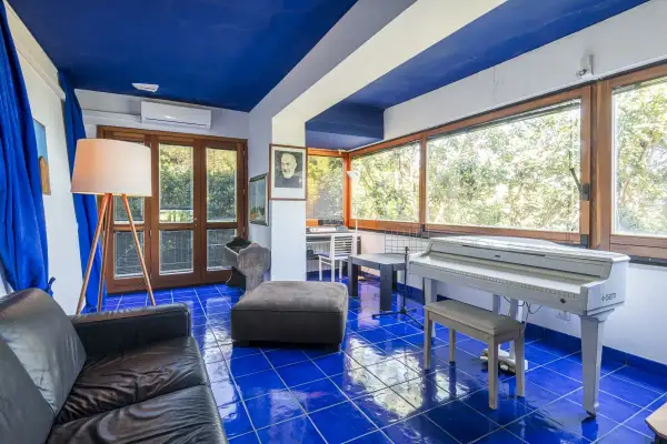Interno con pavimento blu brillante, pianoforte bianco, divano nero e un ritratto di Padre Pio, come in testi lucio dalla la casa in riva al mare.