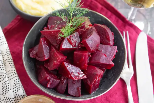Schüssel mit gewürfelten, glänzenden roten Rüben, die man roh essen kann, garniert mit Dill. Daneben Kartoffelpüree und Besteck.