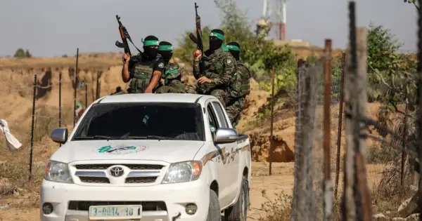 Uzbrojeni bojownicy Hamas w zielonych opaskach na głowach siedzą na białej toyocie, gotowi do akcji.