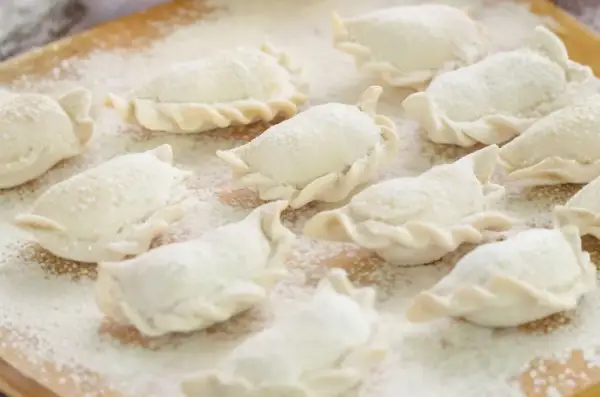 Surowe pierogi, gotowe do gotowania, posypane mąką. Idealne na domowy obiad, zgodnie z tradycyjnym ciasto na pierogi przepisem.