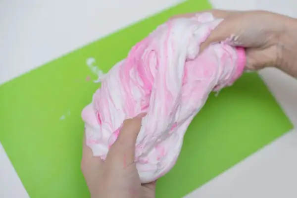 Ręce ugniatają różowo-biały slime, pokazując, jak zrobić slime z kleju i aktywatora.