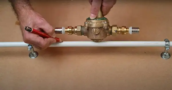 Ajustement d'un réducteur de pression pour comment augmenter la pression d'eau. Un homme marque un tuyau avec un crayon.