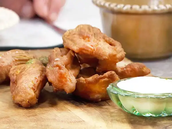 Krispiga, gyllene friterade zucchiniblommor med en klick vit dippsås på en träskärbräda.