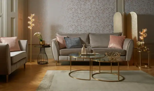 Przytulny salon glamour z szarą sofą, różowymi poduszkami i złotymi dodatkami.